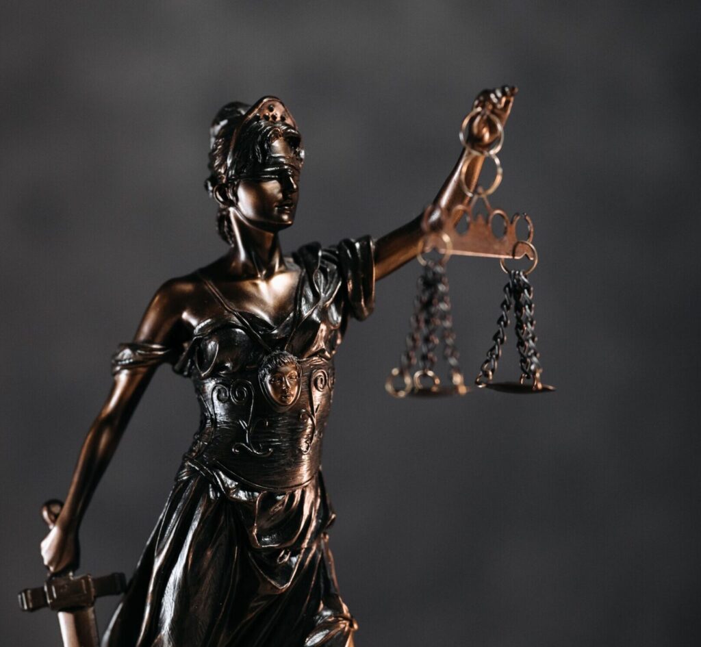 Detailed bronze Lady Justice statue with scales and sword against a dark background, symbolizing law and justice.